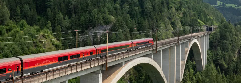 Roter Zug, der auf einer Brücke über das Gebirge fährt